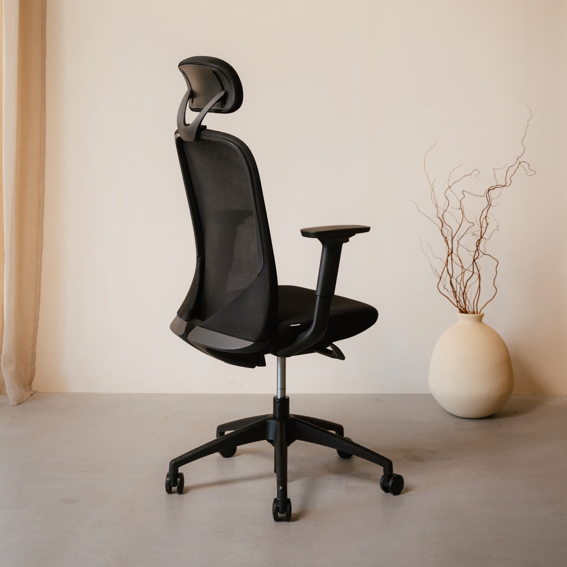 Black office chair in a minimalistic room with a vase and plant.